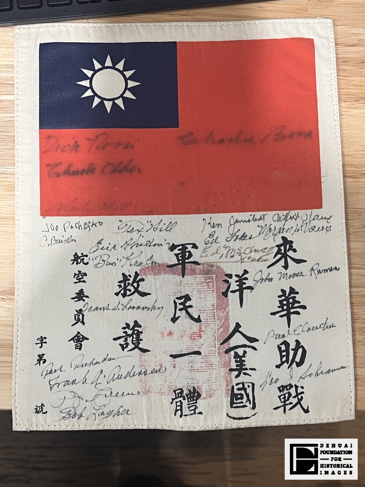 TFA-CA-122 — The blood chit: the flag of the Republic of China, the printed sentence 來華助戰洋人（美國）軍民一體救護 [this foreigner (an American) has come to China to help in the war; soldiers and civilians alike, rescue and protect him], the 航空委員會 [Aeronautical Affairs Commission] line with its blank serial, the rubbed red rectangle at the centre, and twenty-two signatures. Several signatures on the red field are faint against the printed ground.
